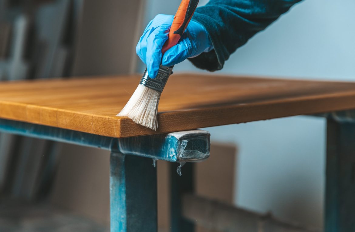 coating of wooden surface with protective varnish. hand in blue rubber glove uses brush coating of wooden surface with protective varnish. hand in blue rubber glove uses brush.