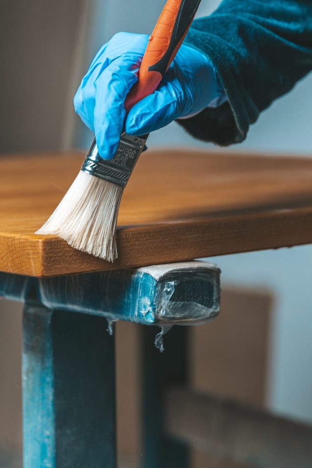 coating of wooden surface with protective varnish. hand in blue rubber glove uses brush.